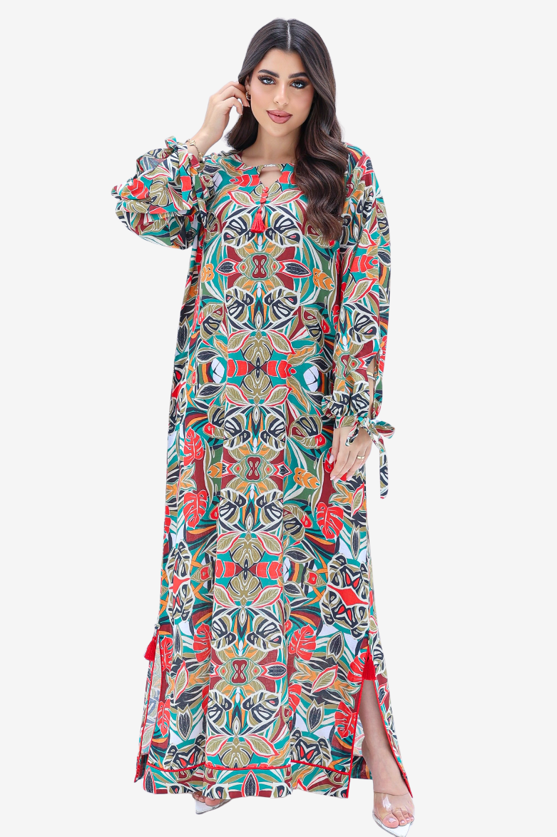 A woman modeling a long-sleeved maxi dress with a vibrant, multicolor symmetrical geometric and floral print. The dress features a round neckline, tie details at the cuffs, and side slits, shown against a plain light gray background.
