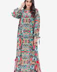 A woman modeling a long-sleeved maxi dress with a vibrant, multicolor symmetrical geometric and floral print. The dress features a round neckline, tie details at the cuffs, and side slits, shown against a plain light gray background.