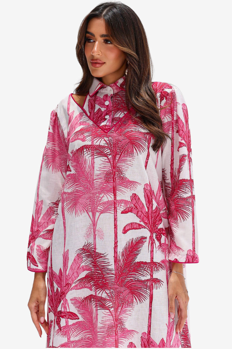 A woman wearing a long-sleeve collared dress with a pink palm tree print on a white background, photographed against a light gray studio backdrop.