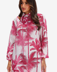 A woman wearing a long-sleeve collared dress with a pink palm tree print on a white background, photographed against a light gray studio backdrop.