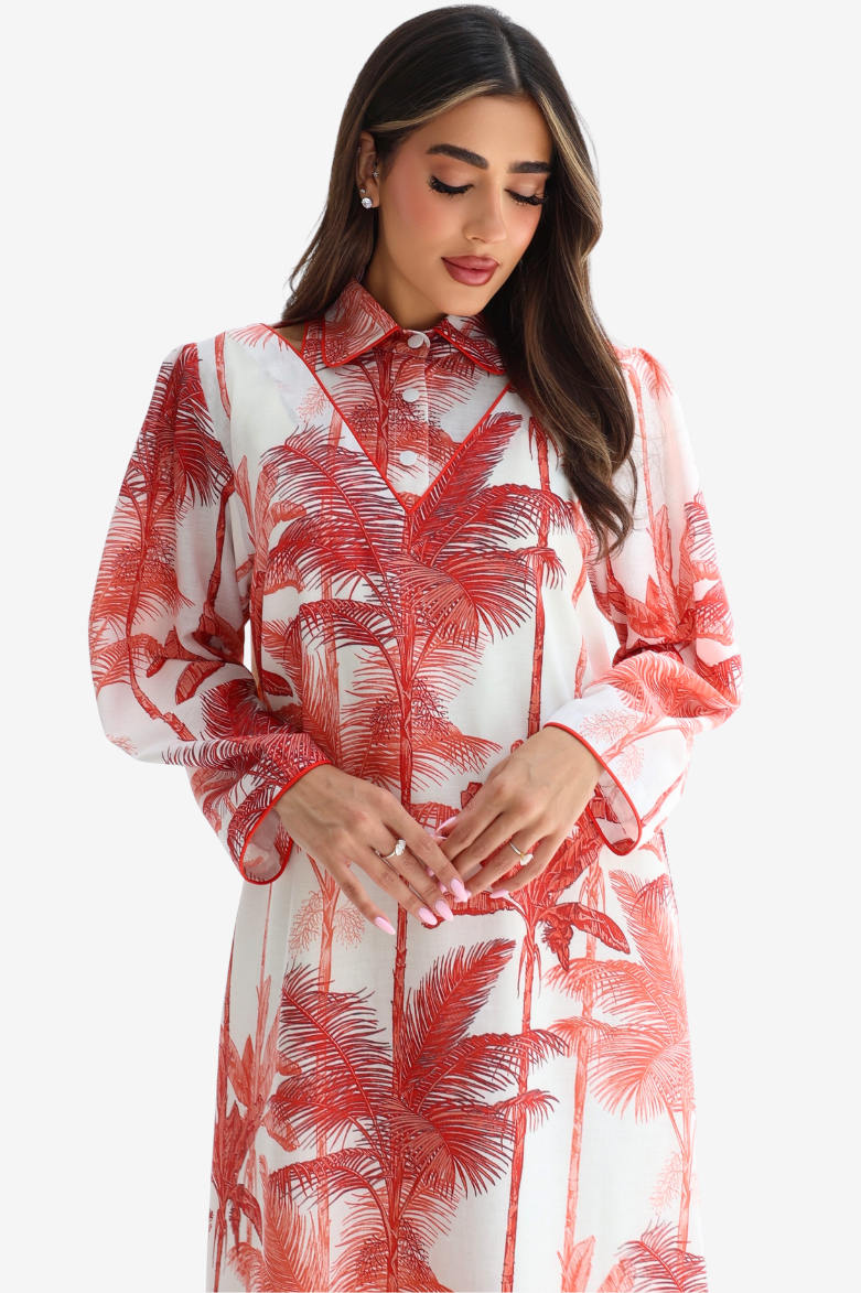 A woman wearing a long-sleeve collared dress with a red palm tree print on a white background, photographed against a light gray studio backdrop.