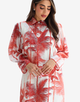 A woman wearing a long-sleeve collared dress with a red palm tree print on a white background, photographed against a light gray studio backdrop.