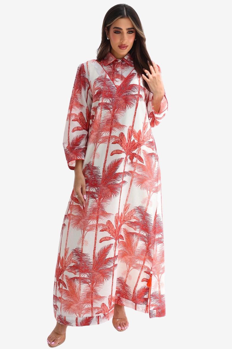 A woman modeling a long-sleeved, collared maxi dress with a red palm tree print on a white background, set against a plain light gray studio backdrop.