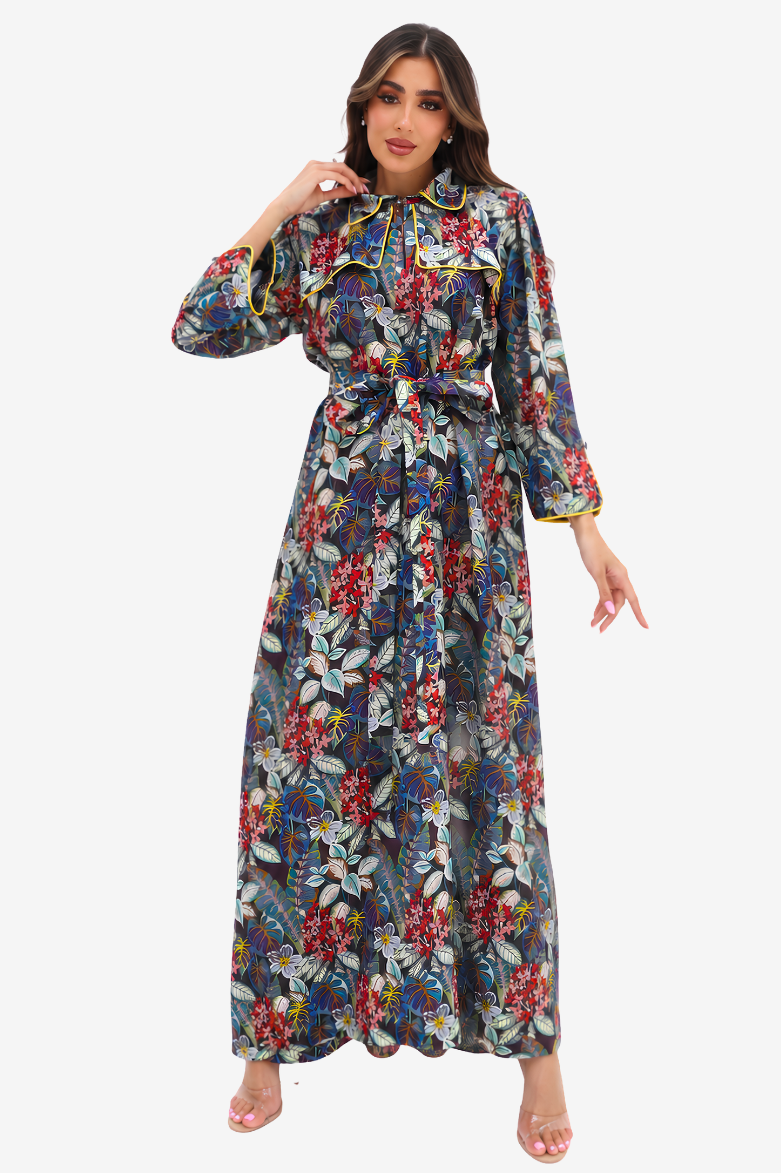 A woman modeling a long-sleeved maxi dress with a dark blue-gray base and a vibrant multicolor floral print, featuring a tie-neck detail and a matching waist tie, set against a plain light gray background.