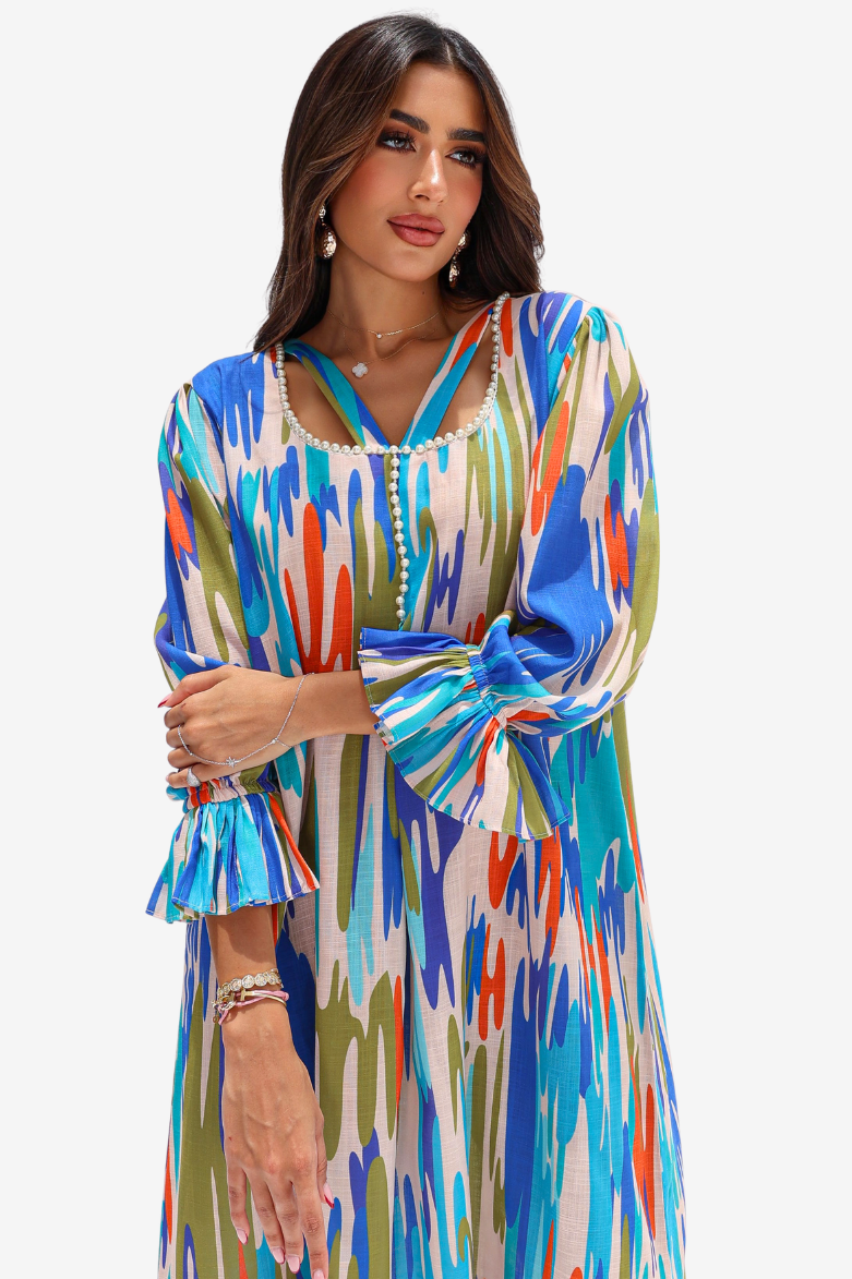 A woman modeling a long-sleeve kaftan dress with a vibrant multicolor ikat pattern in blue, green, orange, and beige on a white background.