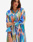 A woman modeling a long-sleeve kaftan dress with a vibrant multicolor ikat pattern in blue, green, orange, and beige on a white background.