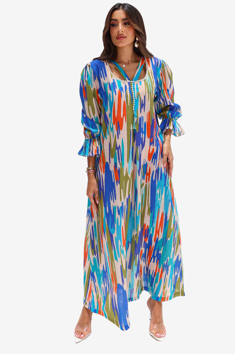 A woman modeling a long-sleeve maxi dress with a vibrant multicolor ikat pattern in shades of blue, orange, green, and white, set against a plain light gray background.