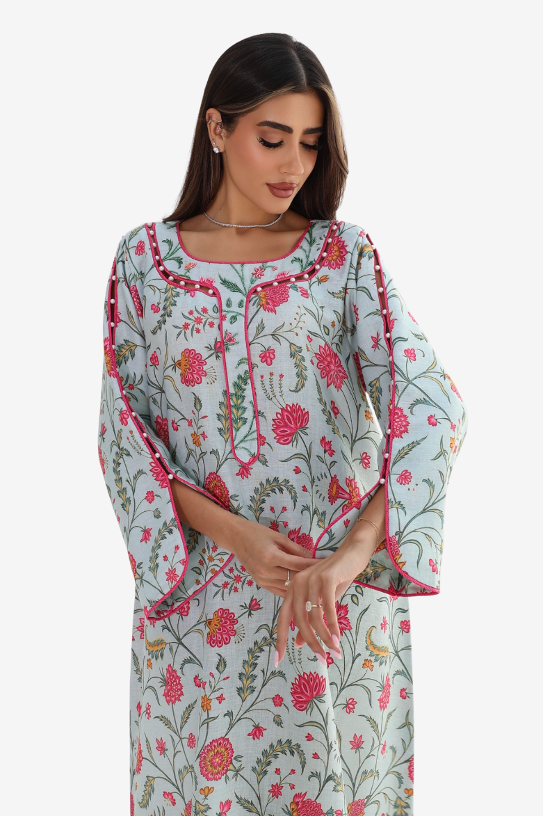 A woman wearing a light blue-green printed kurta with pink and red floral patterns and pink piping details, photographed against a plain light gray background.