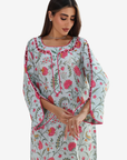 A woman wearing a light blue-green printed kurta with pink and red floral patterns and pink piping details, photographed against a plain light gray background.