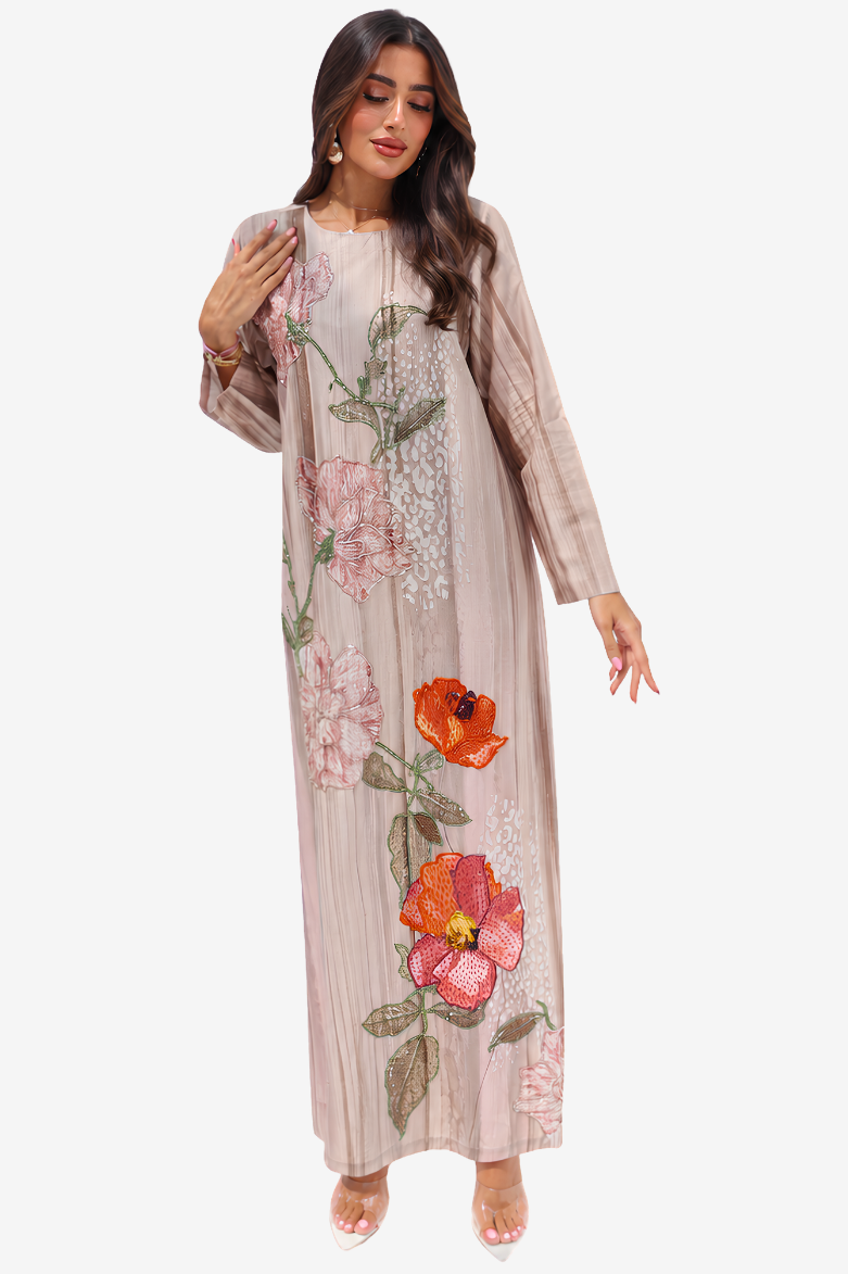 A woman modeling a long, loose-fitting beige maxi dress with pink and orange floral embroidery and sequin detailing, set against a plain light gray background.