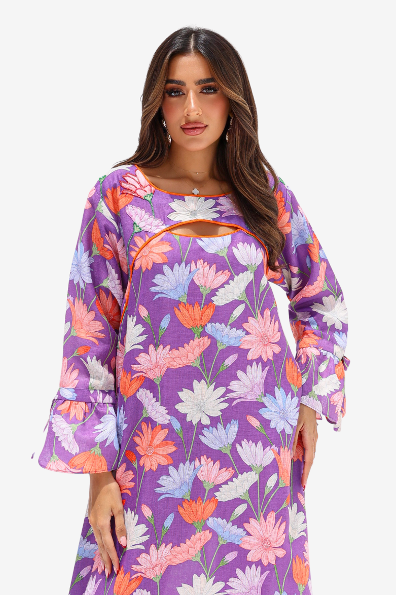 A woman modeling a purple long-sleeve dress with a colorful floral print, featuring a keyhole cutout at the chest, against a plain light gray background.