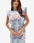 A woman modeling a sleeveless midi dress with a colorful floral print in shades of blue, pink, purple, and white, featuring structured shoulder details and a gathered waist.