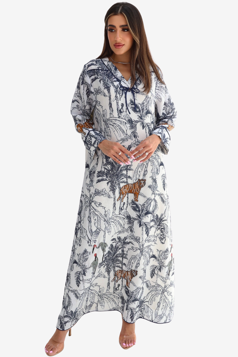 A woman modeling a long-sleeve maxi dress with a blue and brown jungle print on a white background, featuring a tie-neck detail and cutout sleeves.