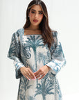 Woman wearing a white dress with blue palm tree patterns on a white background